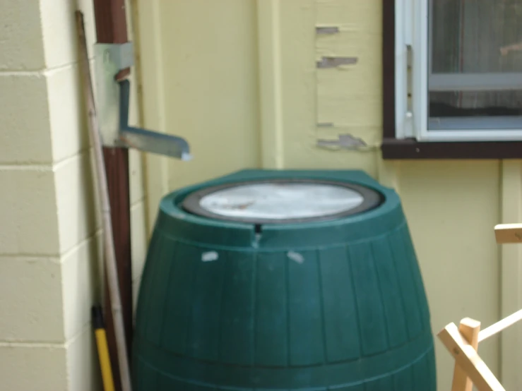 a green barrel sitting outside of a building with a window