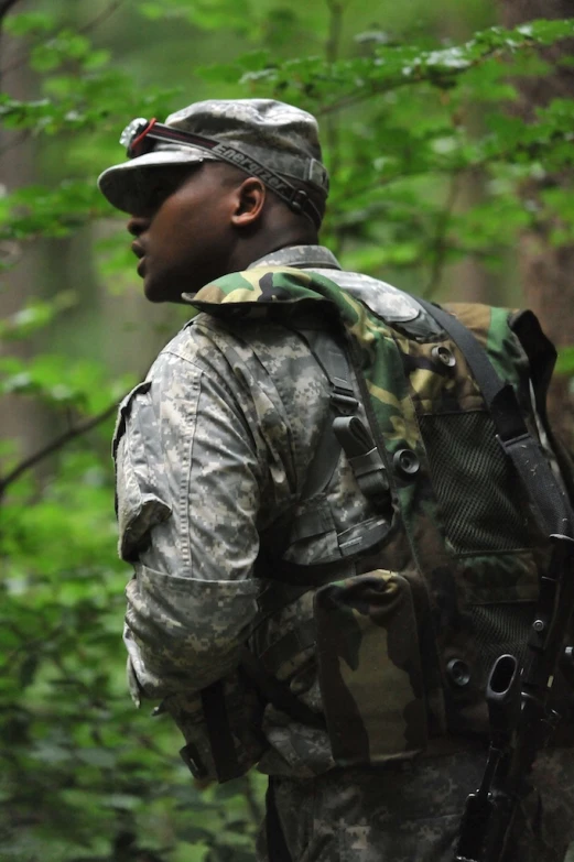 the man is carrying an army gun and hunting pack