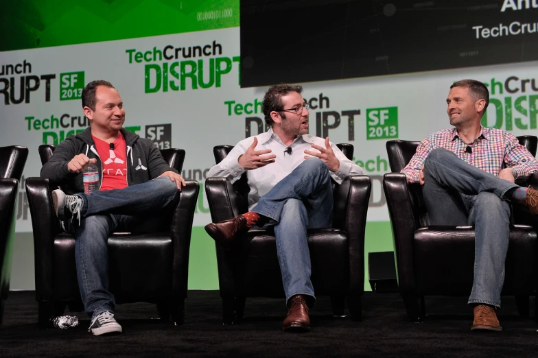 three men sitting on chairs during a panel