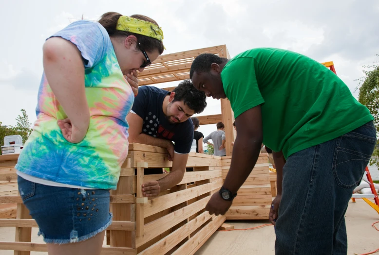 three young people in colorful shirts and jeans looking over a wooden fence