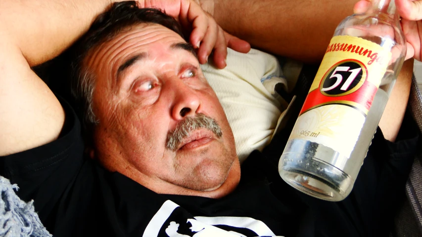 a man lays on the couch while holding an unopened drink