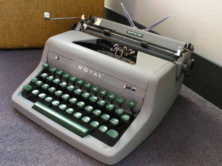 an old style green typewriter sitting on a grey floor