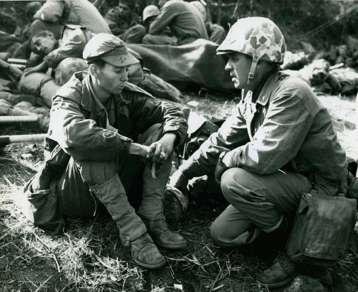 two soldiers talking while sitting next to another soldier