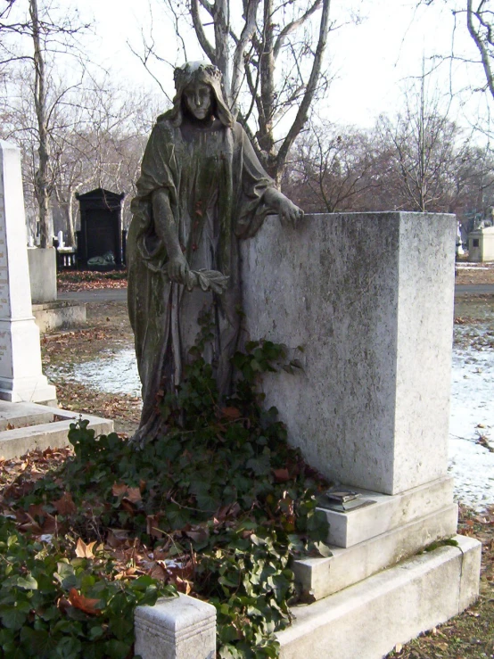 a statue of a woman with hands in her pockets sitting next to a grave