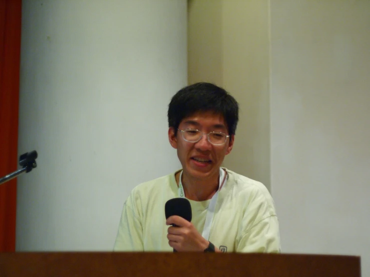 a man wearing glasses talking to someone at a podium