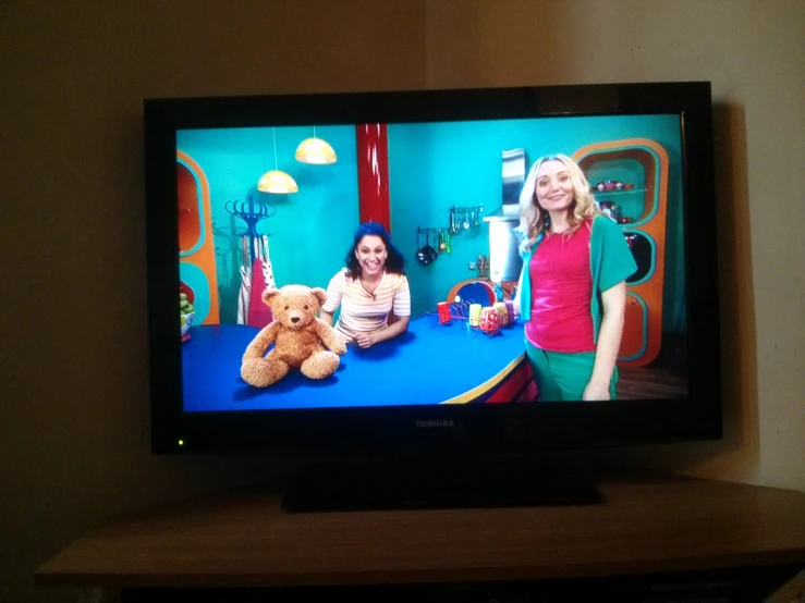 television showing two women with a teddy bear on the right