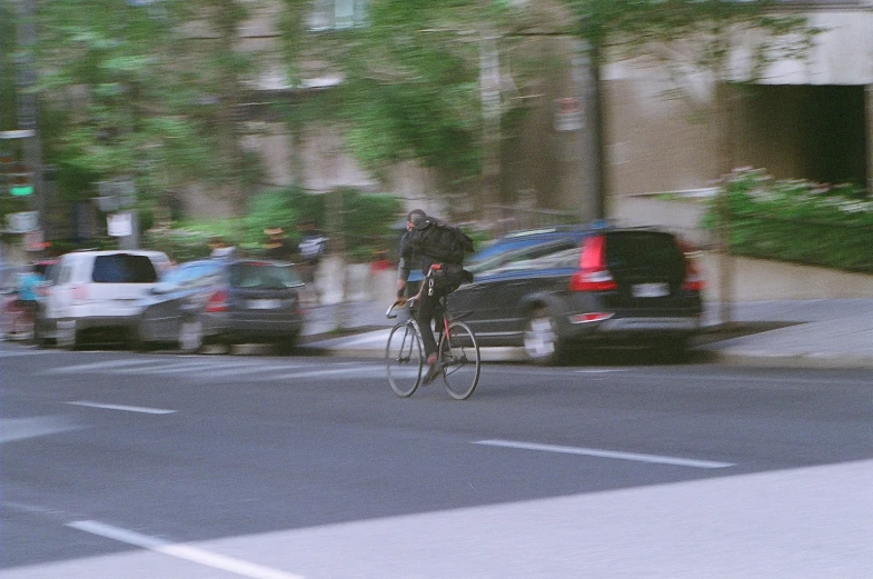 man on bicycle riding next to parked cars and trees