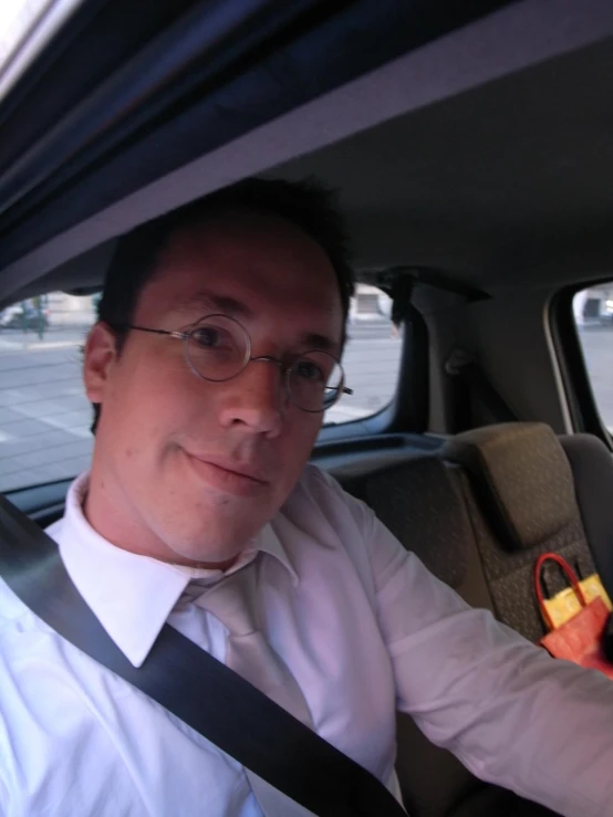 a man in glasses and a white shirt sitting inside of a car