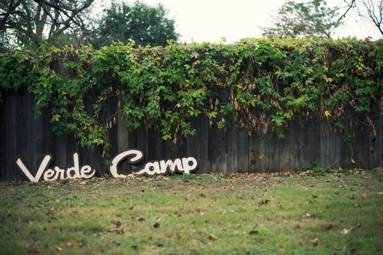 a po of the word vordercomm painted on a fence in front of a field with a fence covered in vines