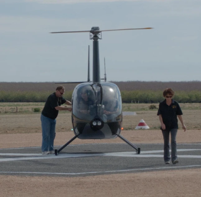 two people standing next to a helicopter on a runway