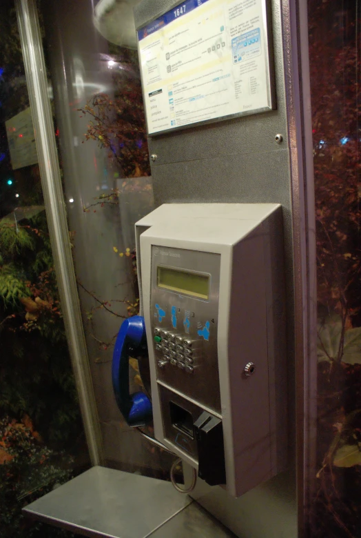 a modern public pay phone sitting in front of a window