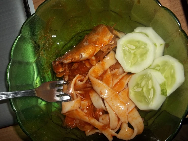 a bowl is full of noodles, sliced cucumbers and meat