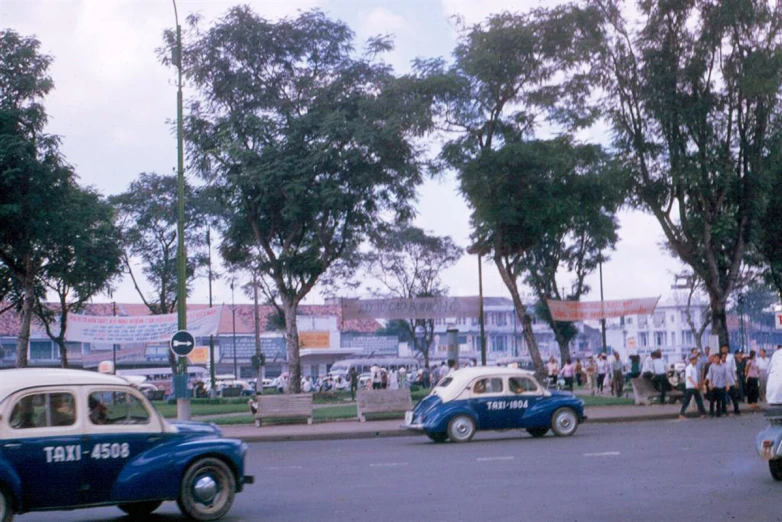 two vintage cars, an old one and some people in the background