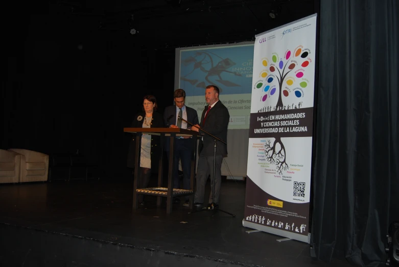 two men stand at a podium and talk with a speaker