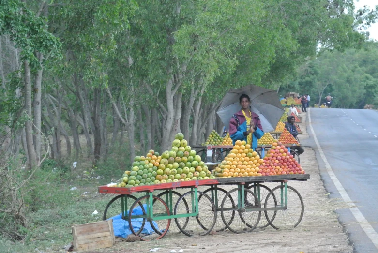 people selling fruit on carts next to an asphalt road