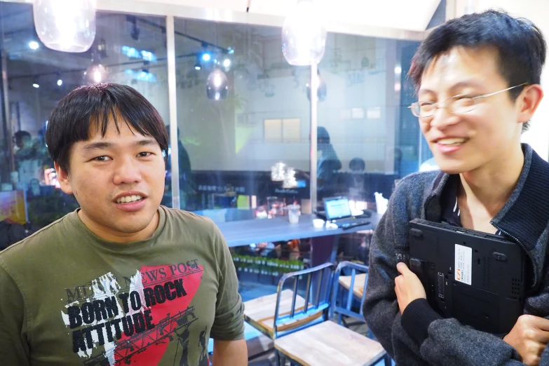 two asian men smiling while holding up a camera