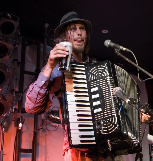 a man in fedora standing at a microphone holding an accordion