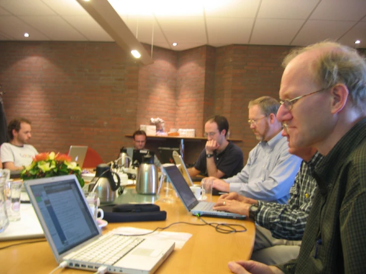 men are working on computers at a table in a conference room