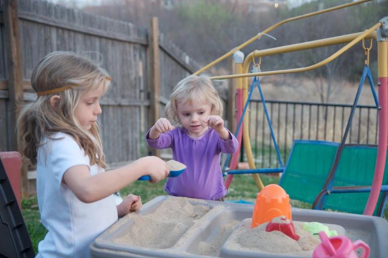 two girls play in a sandbox and on the swings