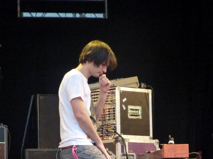 a guy in white t - shirt standing on stage at outdoor concert