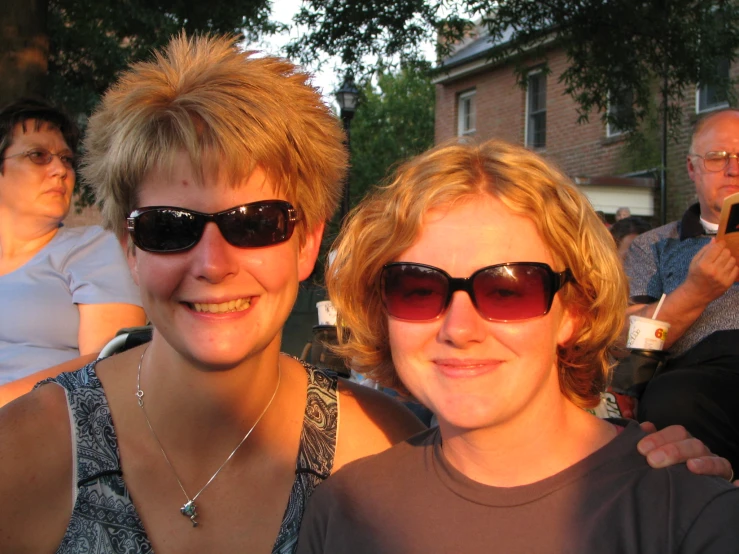 two women in dark sunglasses stand together at a group po