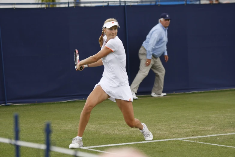 female tennis player in white playing in an outdoor tennis court