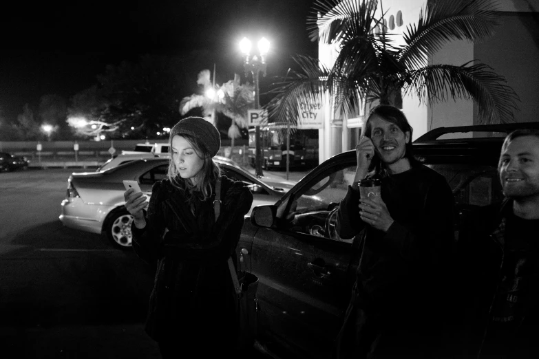 three young women at night drinking beverages in a parking lot