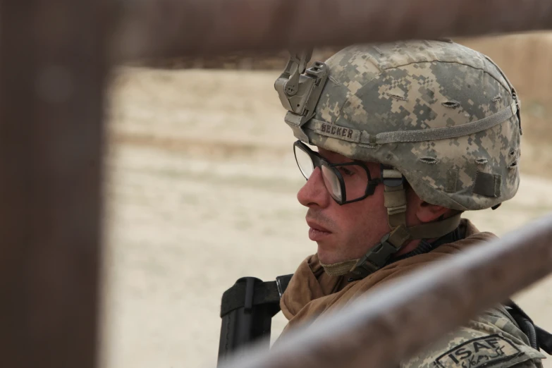 a man in camouflage gear stares out from behind a wooden wall