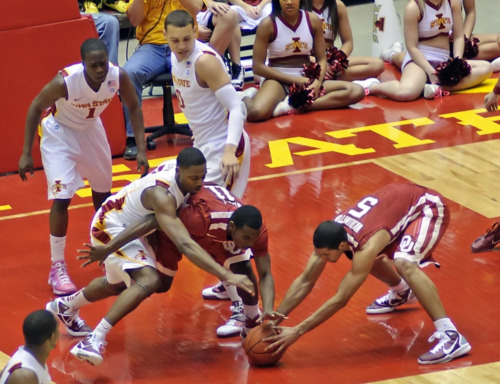 players in red and white wear red and white jerseys as they play basketball while an audience watches them from their seats