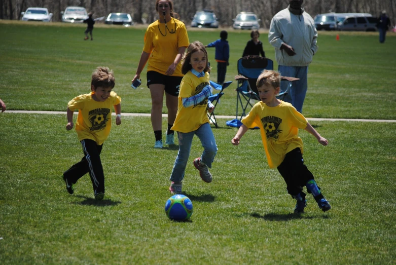 small children in yellow shirts are playing with a ball