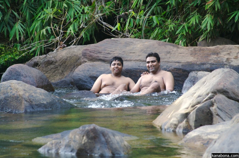 two young men sitting in the water, one looking at the camera