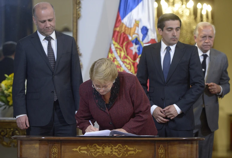 a woman in glasses and a suit is signing papers