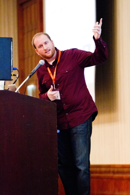 a man in a red shirt speaking at a podium