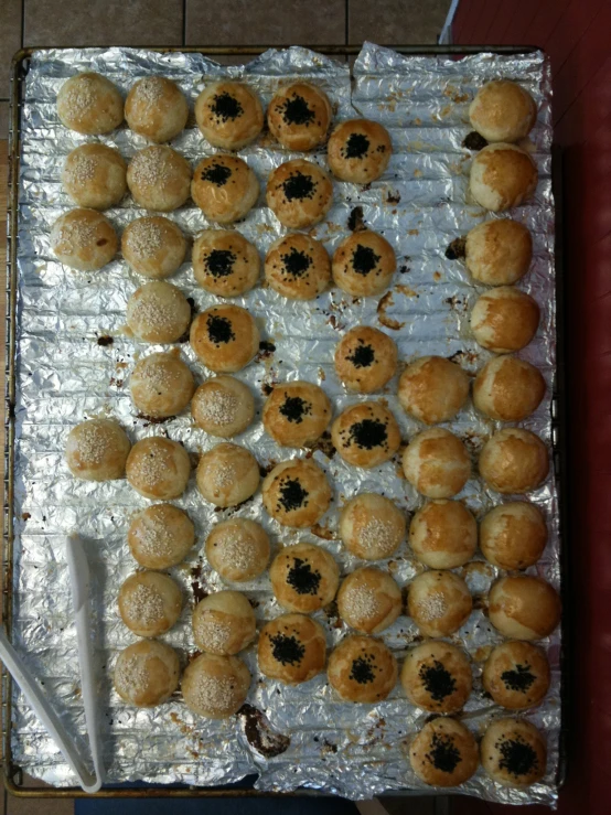 doughnuts sitting on aluminum sheet lined up on top of a pan