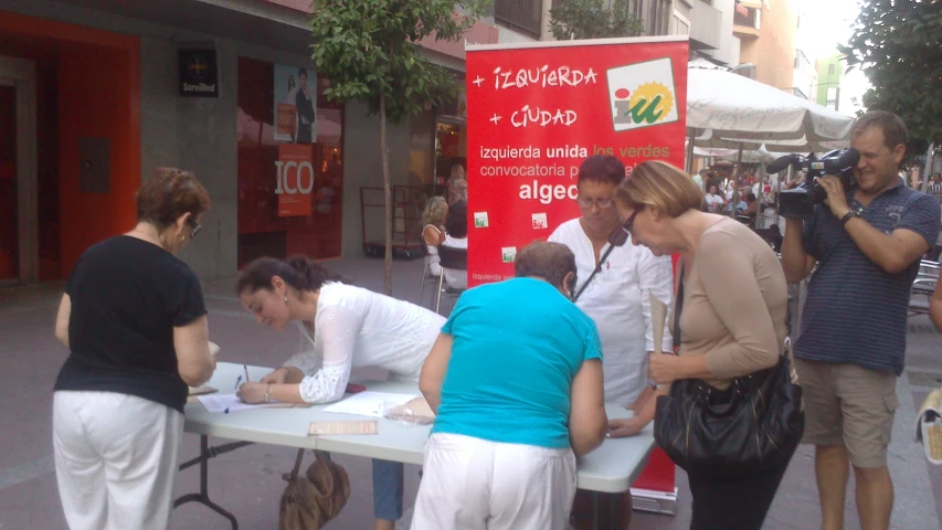 people writing letters at a table in front of a food stand