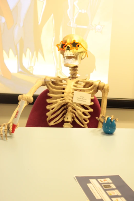 a skeleton sits behind a podium in front of a screen