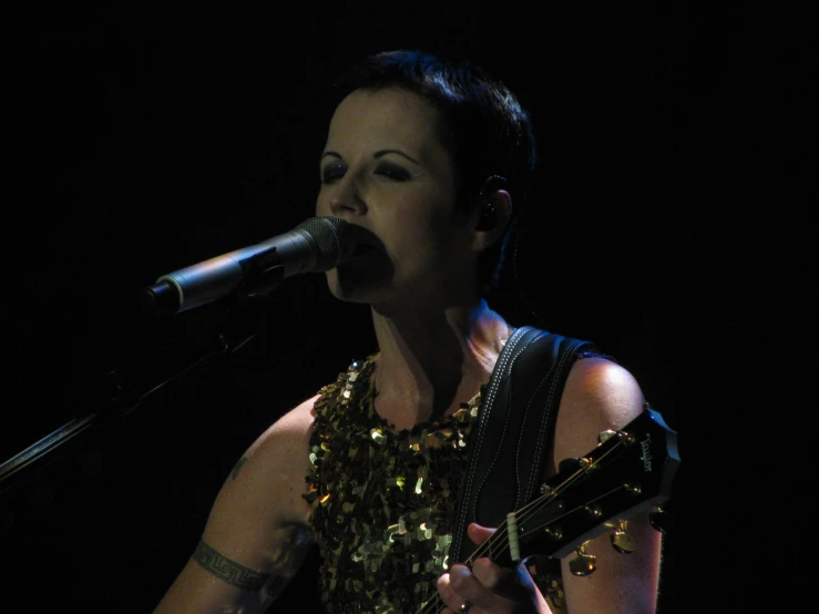 the woman is holding her guitar on stage and singing into a microphone