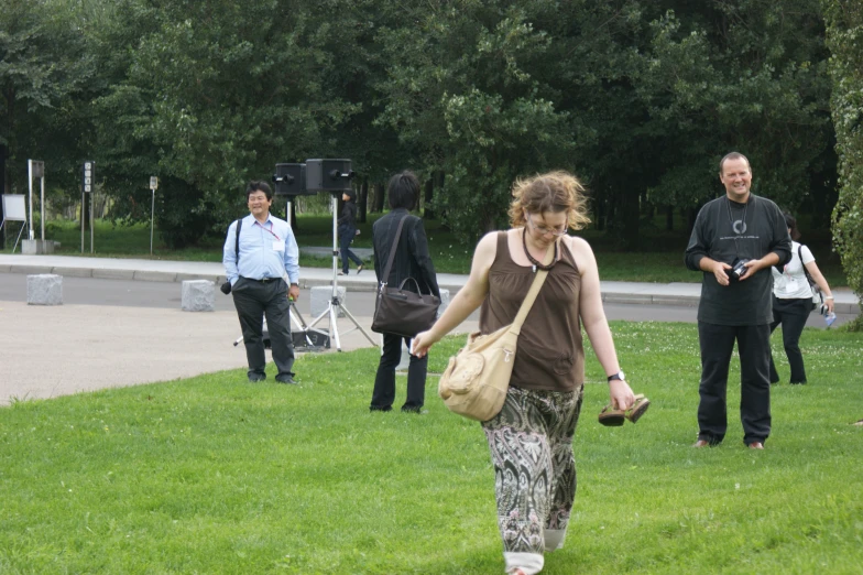 people are walking on the grass while one is carrying a handbag
