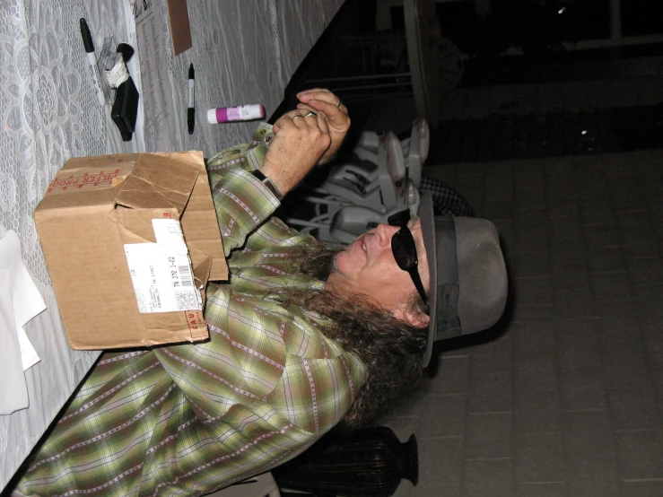 man in plaid shirt and fedora with box around table