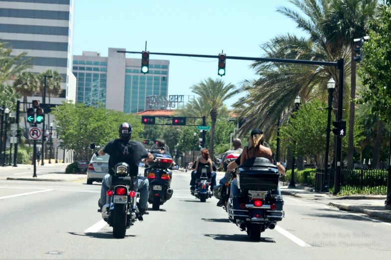 many people riding motorcycles on the street near palm trees