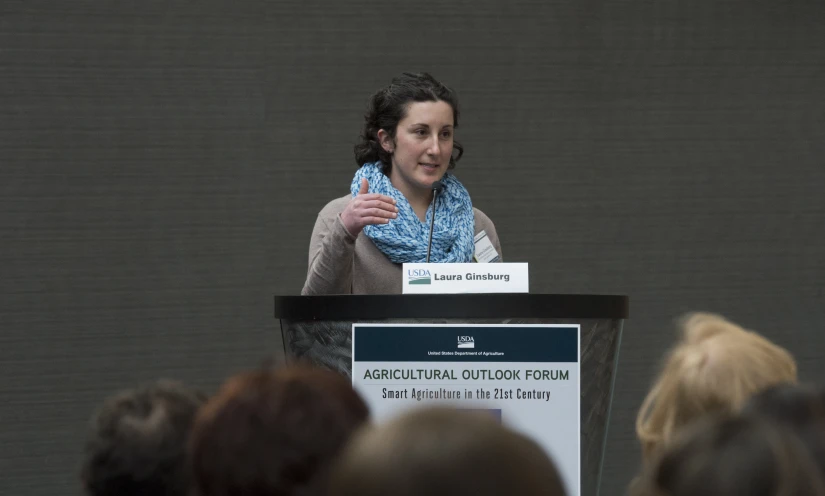 a woman is at a podium talking in front of a crowd