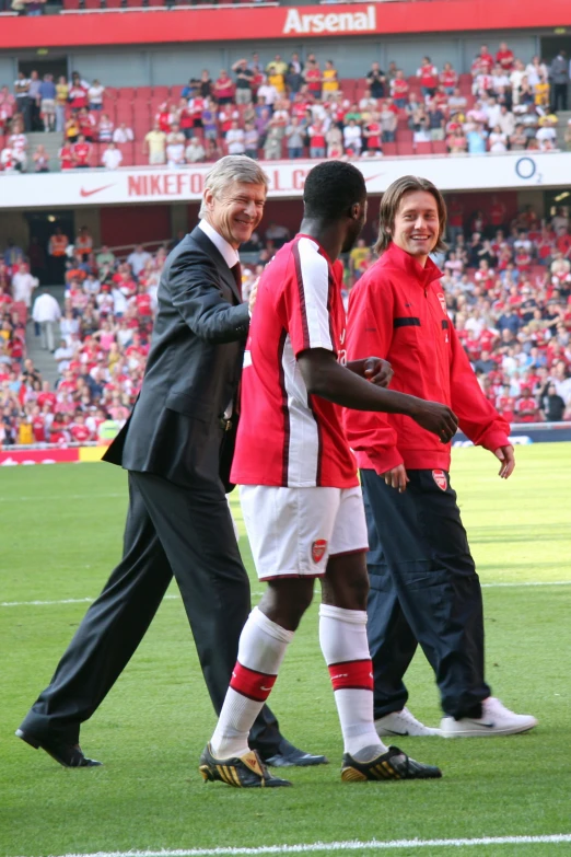 two men shaking hands with a soccer player in red and white