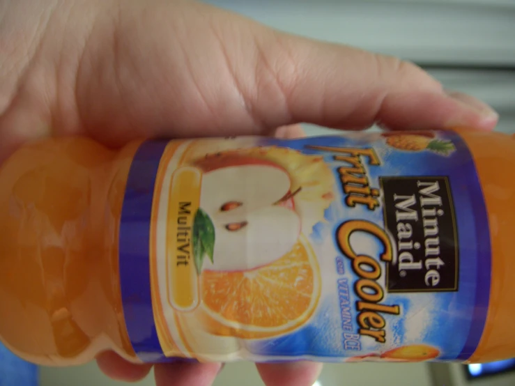 a hand holding onto an orange drink with its lid open