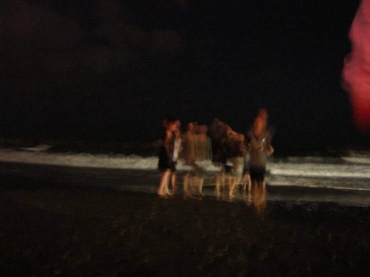 a group of people standing on the beach at night