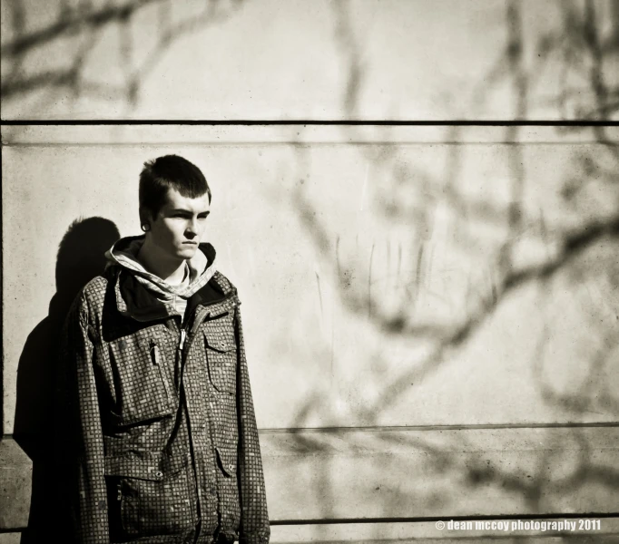 a young man poses against a wall and casting a shadow on the side