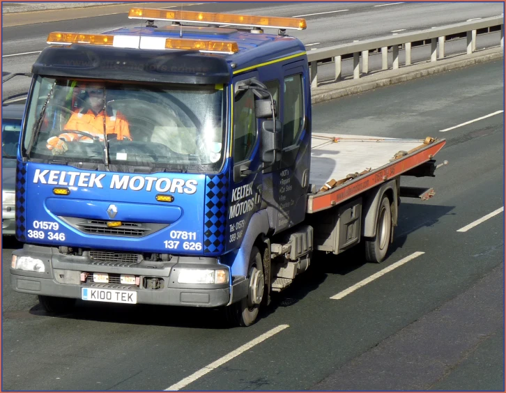 a flatbed truck driving on the road with a few men in front