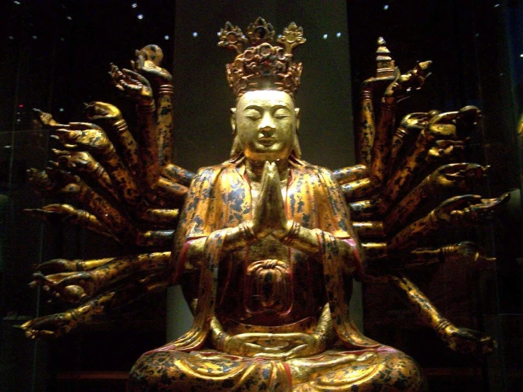 a gold statue of buddha with three hands in the shape of the figure of a peacock