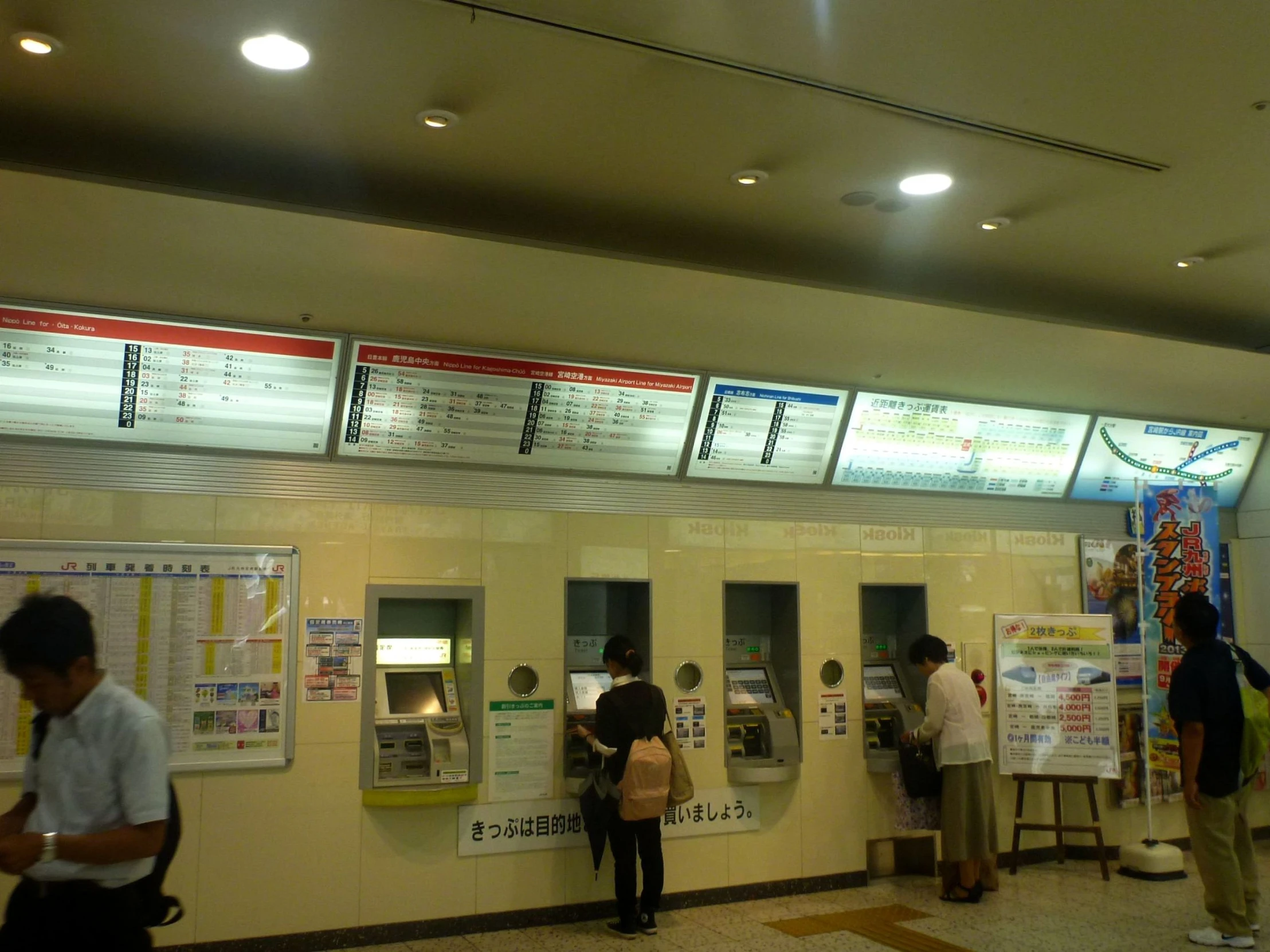 people stand at a row of vending machines in an asian station