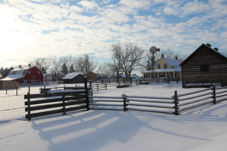 a farm in the snow with a fence and two barns