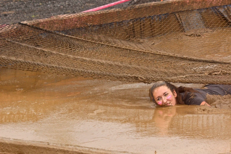 a girl lies in the mud, surrounded by netting